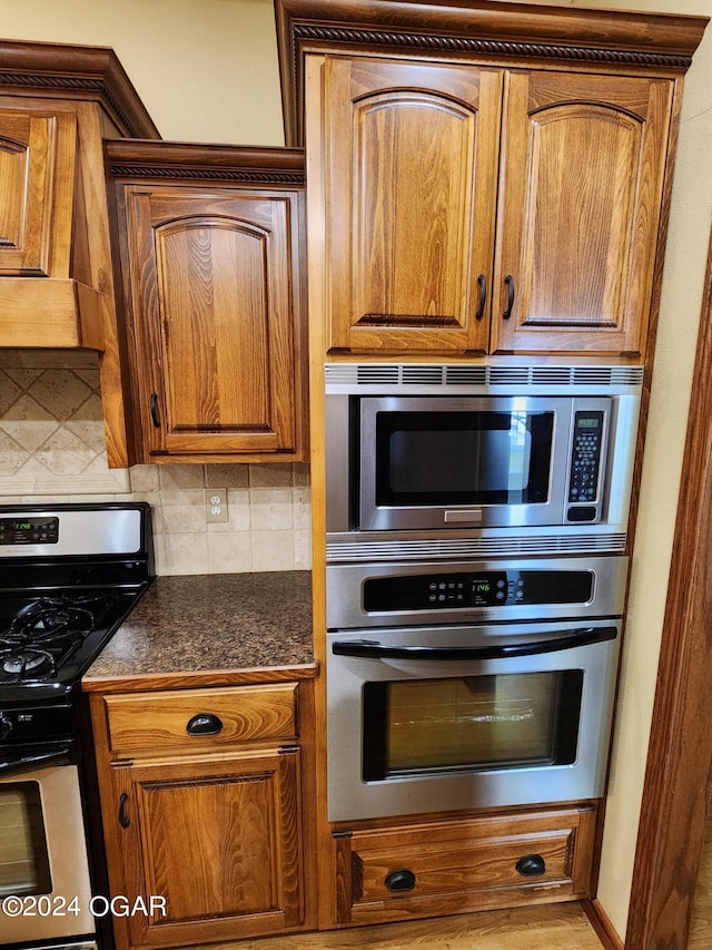 305 E Maple St, Liberal, MO 64762 - kitchen featuring appliances with stainless steel finishes, dark countertops, brown cabinetry, and backsplash