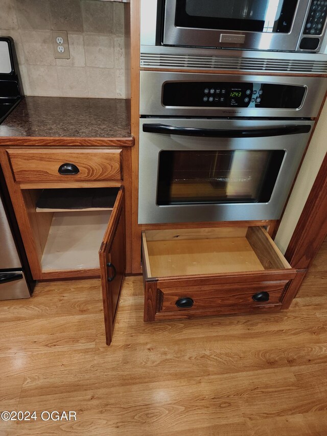 305 E Maple St, Liberal, MO 64762 - interior details featuring tasteful backsplash, brown cabinetry, appliances with stainless steel finishes, dark countertops, and light wood-type flooring