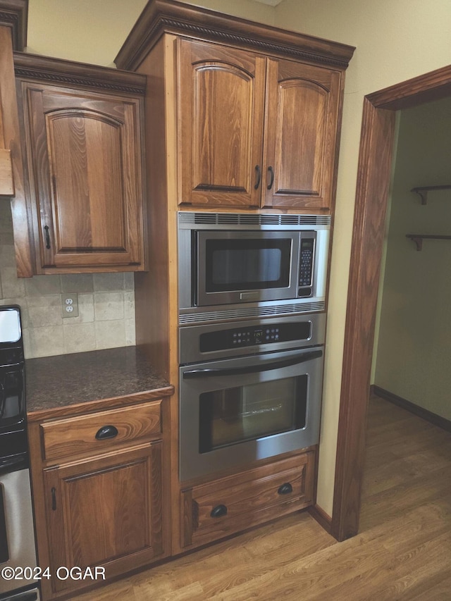 305 E Maple St, Liberal, MO 64762 - kitchen with stainless steel microwave, double oven, backsplash, light wood finished floors, and baseboards