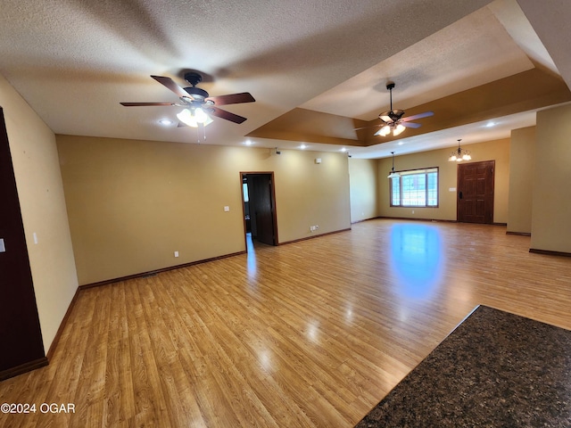 305 E Maple St, Liberal, MO 64762 - unfurnished living room featuring baseboards, light wood-style floors, a raised ceiling, and ceiling fan with notable chandelier
