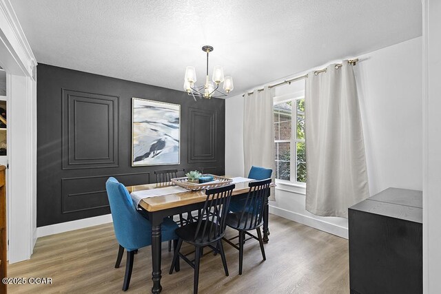 dining room with light wood-style flooring, a chandelier, baseboards, and a textured ceiling