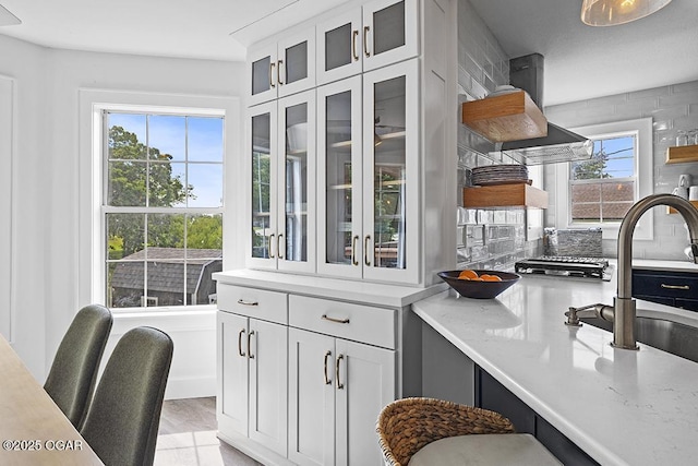 kitchen with open shelves, a sink, glass insert cabinets, white cabinets, and light stone countertops