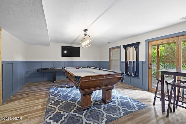 recreation room featuring light wood-style floors, a wainscoted wall, pool table, a textured ceiling, and a decorative wall