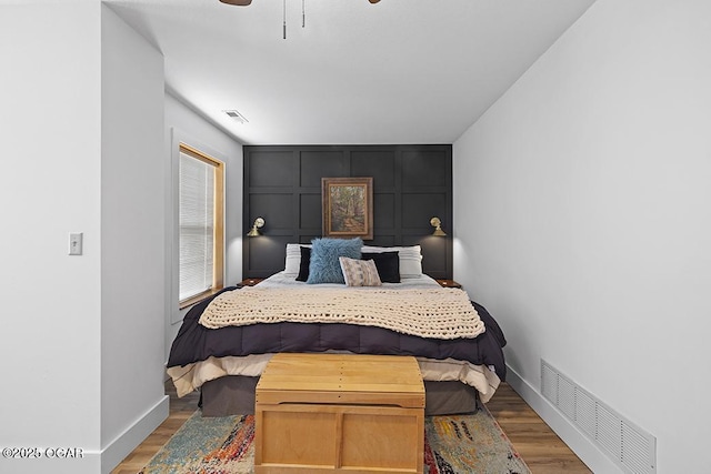 bedroom featuring wood finished floors, a decorative wall, baseboards, and a ceiling fan