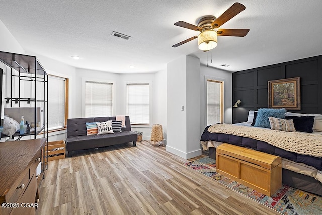 bedroom with light wood-type flooring, baseboards, a textured ceiling, a decorative wall, and ceiling fan