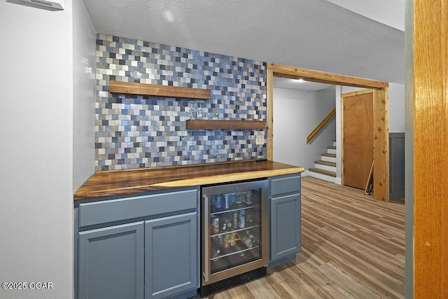 indoor dry bar with wine cooler, stairs, light wood-type flooring, and a textured ceiling