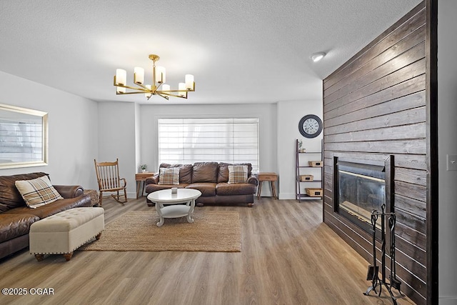 living room featuring a chandelier, wood finished floors, a large fireplace, baseboards, and a textured ceiling