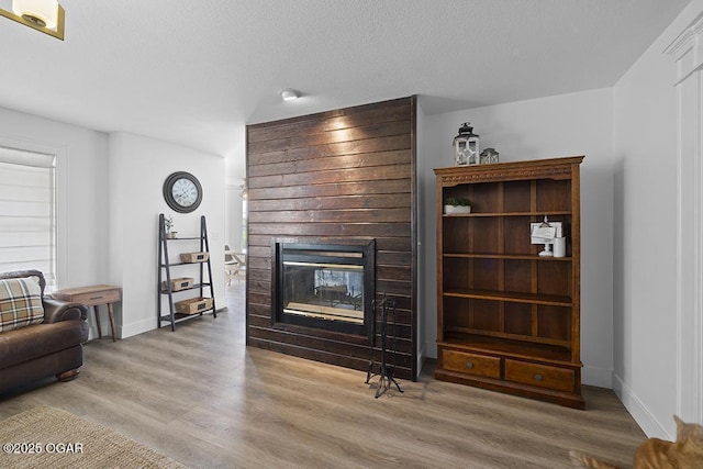 living area with a multi sided fireplace, baseboards, wood finished floors, and a textured ceiling