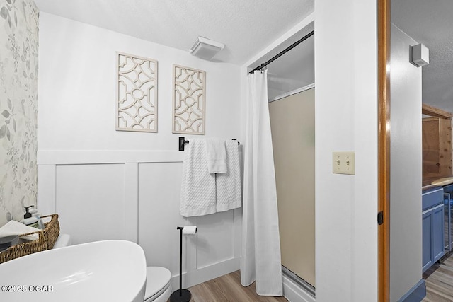 full bathroom featuring wood finished floors, a shower stall, toilet, and a wainscoted wall