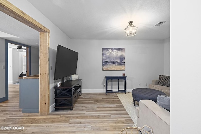 living area featuring wood finished floors, baseboards, ceiling fan, a textured ceiling, and a chandelier