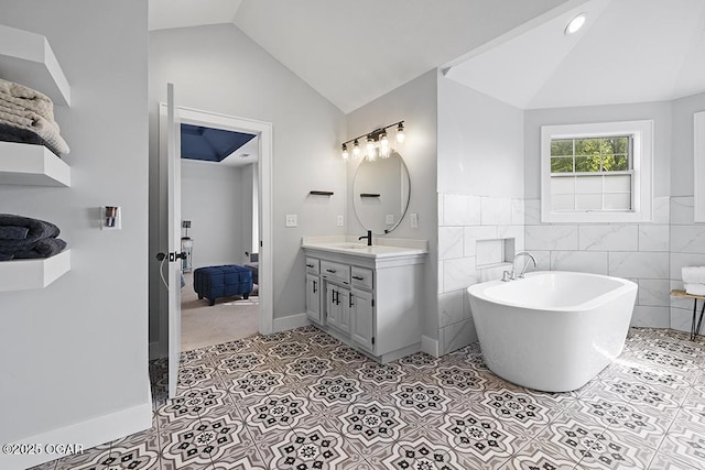 bathroom featuring lofted ceiling, tile patterned floors, tile walls, a freestanding tub, and vanity