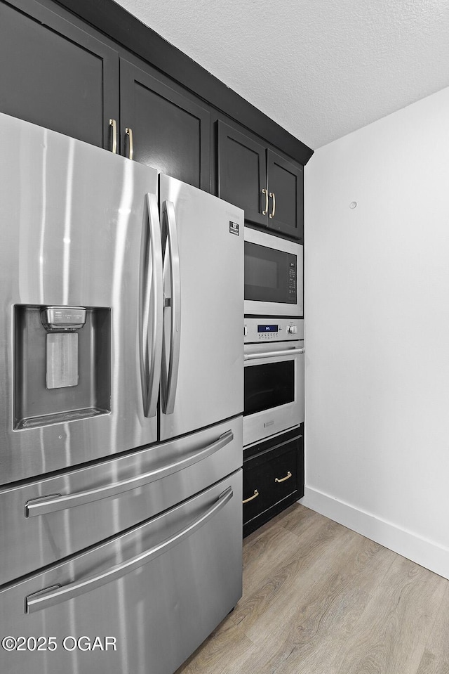 kitchen with stainless steel appliances, light wood-type flooring, baseboards, dark cabinets, and a textured ceiling