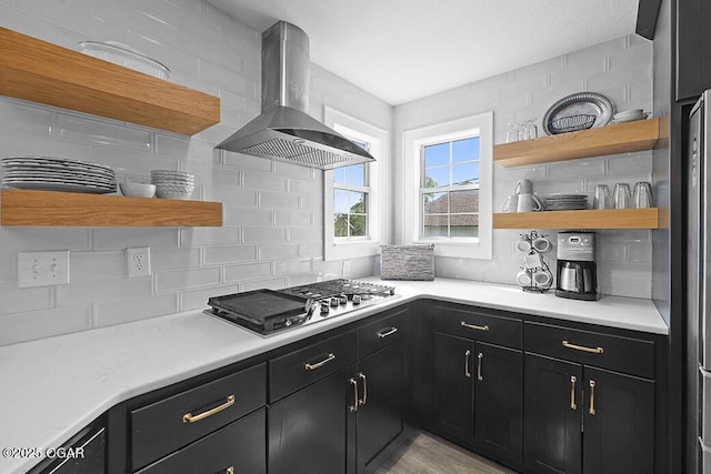 kitchen featuring open shelves, island exhaust hood, dark cabinetry, backsplash, and stainless steel gas stovetop