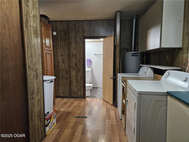105 S Elm St, Mulberry, KS 66756 - clothes washing area featuring wood walls, washer and clothes dryer, light wood-style flooring, gas water heater, and cabinet space