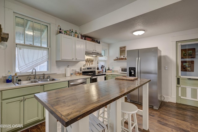 kitchen featuring wooden counters, a sink, under cabinet range hood, green cabinetry, and stainless steel appliances