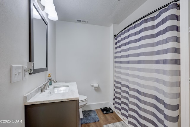 bathroom with a textured ceiling, visible vents, wood finished floors, vanity, and toilet