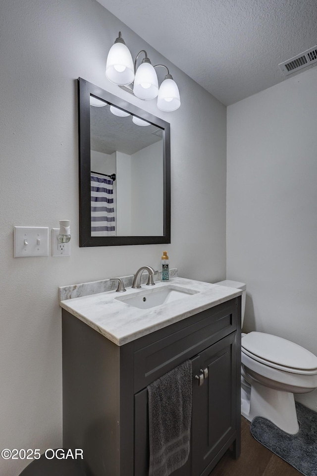 bathroom featuring vanity, toilet, a textured ceiling, wood finished floors, and visible vents
