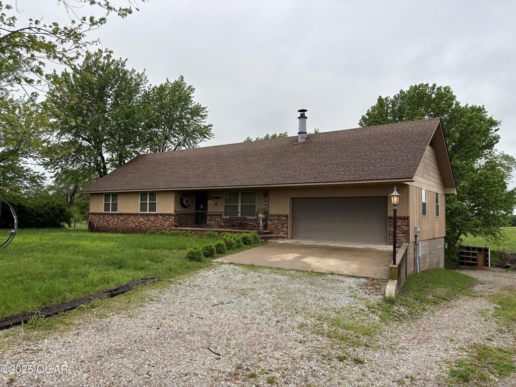1208 S Blackcat Rd, Joplin, MO 64801 - ranch-style home with a front lawn, covered porch, gravel driveway, a shingled roof, and an attached garage