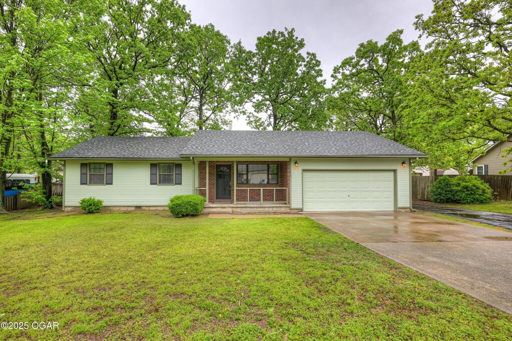 ranch-style home featuring covered porch, driveway, a garage, fence, and a front lawn