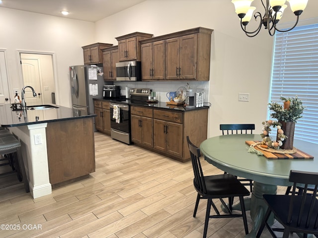 kitchen with dark countertops, a chandelier, a sink, light wood finished floors, and appliances with stainless steel finishes