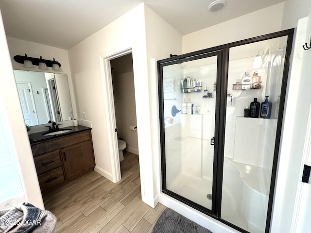 bathroom featuring vanity, toilet, wood finished floors, and a stall shower
