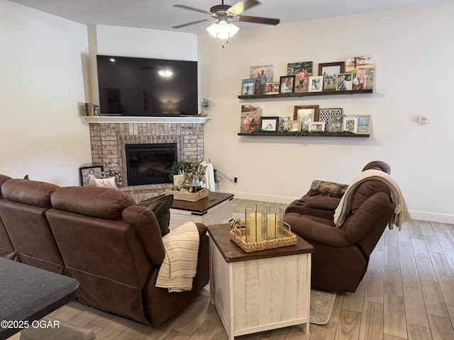 living area with baseboards, a ceiling fan, wood finished floors, and a brick fireplace