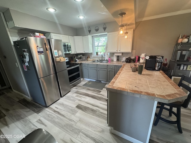 kitchen featuring a sink, light countertops, stainless steel appliances, a peninsula, and ornamental molding