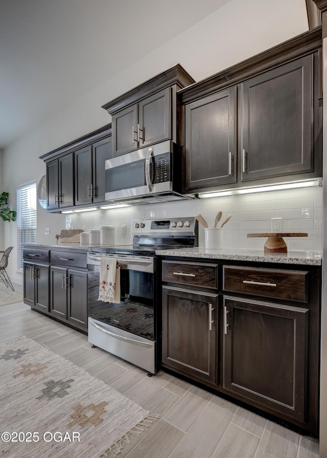 kitchen featuring dark brown cabinetry, light stone countertops, tasteful backsplash, light wood-style flooring, and stainless steel appliances