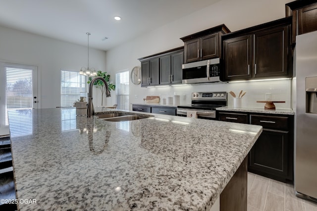 kitchen with light stone countertops, appliances with stainless steel finishes, a center island with sink, and a sink