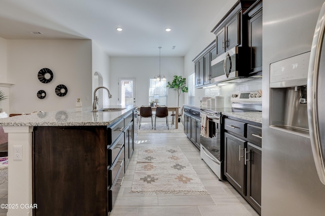 kitchen featuring a center island with sink, recessed lighting, light stone counters, a sink, and appliances with stainless steel finishes