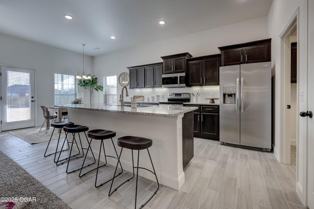 kitchen featuring a kitchen island with sink, a breakfast bar area, light stone countertops, light wood finished floors, and stainless steel appliances