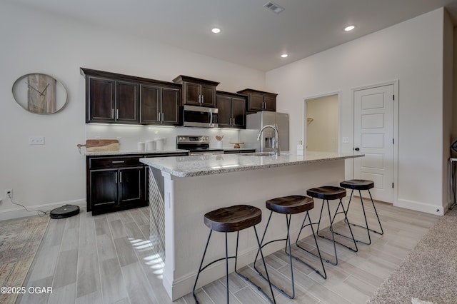 kitchen with a center island with sink, stainless steel appliances, light wood finished floors, and visible vents