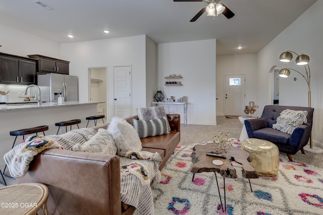 living area featuring a ceiling fan, arched walkways, visible vents, and light carpet
