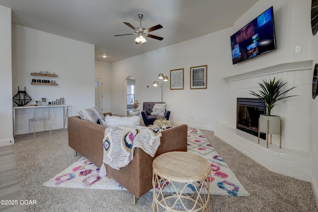 living area with ceiling fan, arched walkways, a fireplace, baseboards, and carpet flooring