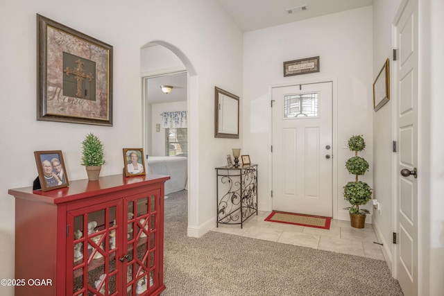 tiled foyer entrance featuring healthy amount of natural light, carpet flooring, arched walkways, and baseboards