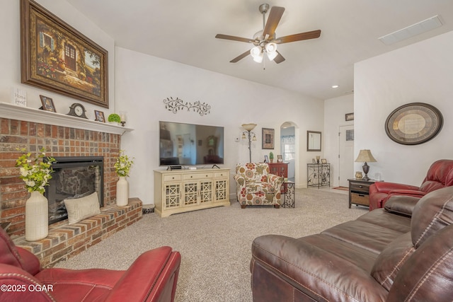 living room with carpet floors, ceiling fan, a brick fireplace, arched walkways, and baseboards