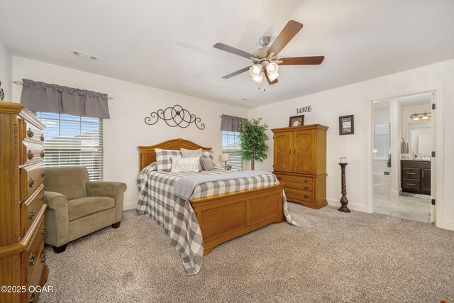 bedroom featuring light carpet, multiple windows, baseboards, and ensuite bathroom
