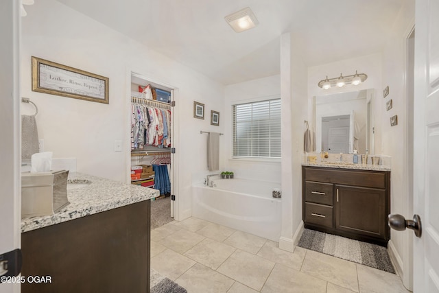 full bath with vanity, a garden tub, a spacious closet, tile patterned floors, and baseboards