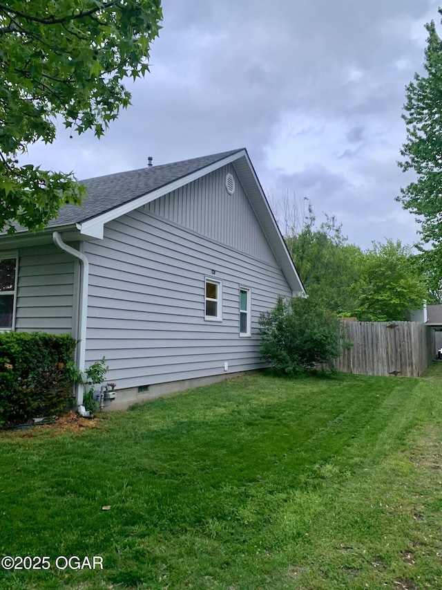 view of side of property featuring a lawn, roof with shingles, and fence