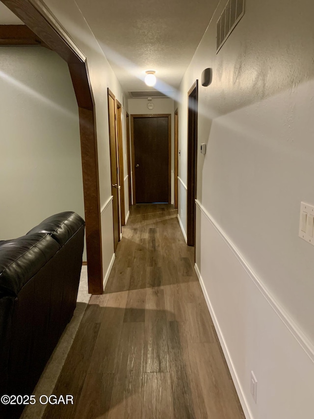 corridor with a textured ceiling, baseboards, visible vents, and wood finished floors