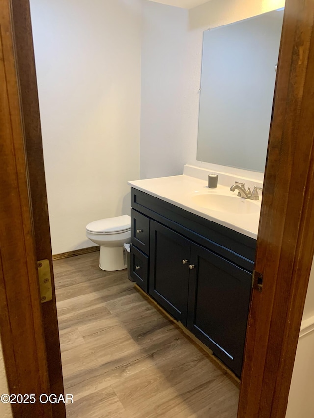 half bathroom with vanity, toilet, and wood finished floors