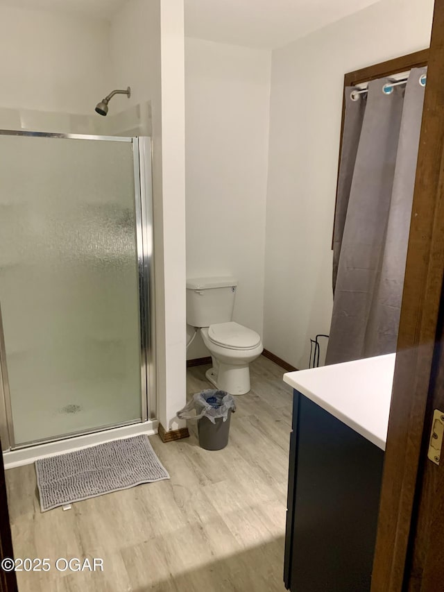 full bath featuring toilet, baseboards, a shower stall, and wood finished floors