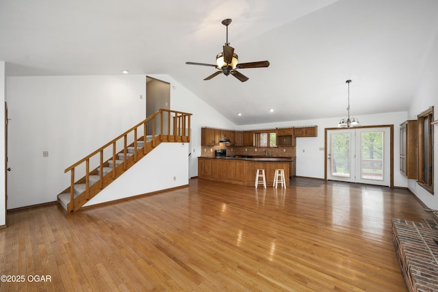unfurnished living room featuring ceiling fan with notable chandelier, stairs, baseboards, wood finished floors, and vaulted ceiling