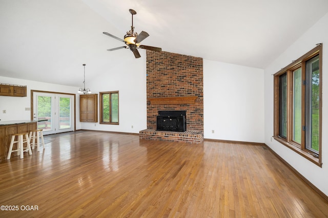 unfurnished living room with a fireplace, baseboards, high vaulted ceiling, light wood finished floors, and ceiling fan with notable chandelier