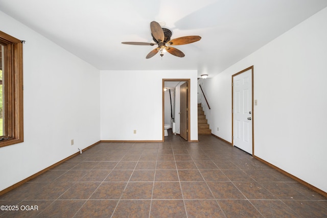 spare room with baseboards, ceiling fan, stairway, and dark tile patterned flooring