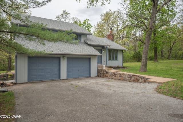 tri-level home featuring a shingled roof, a garage, a front yard, a chimney, and driveway