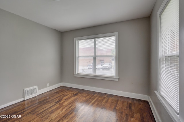 empty room featuring dark wood finished floors, visible vents, and baseboards