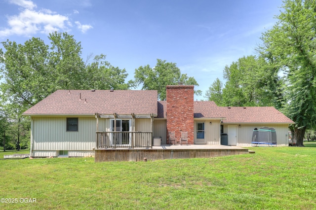 400 Silverwood Ln, Joplin, MO 64801 - rear view of house featuring a trampoline, a chimney, a yard, a wooden deck, and roof with shingles