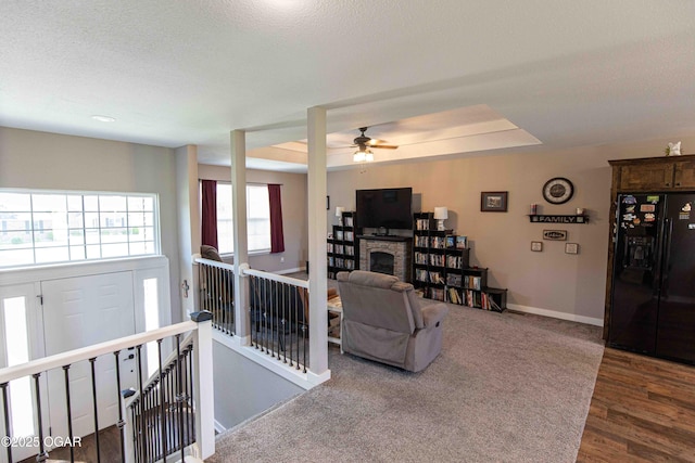 living area featuring wood finished floors, a fireplace, baseboards, a raised ceiling, and ceiling fan