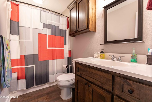 bathroom featuring toilet, vanity, a textured wall, and wood finished floors